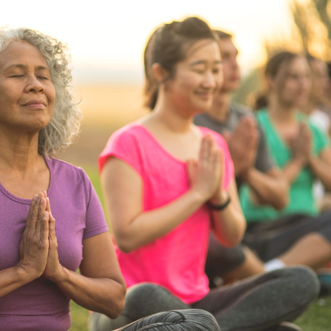 sunset yoga group outside meditating in prayer hands