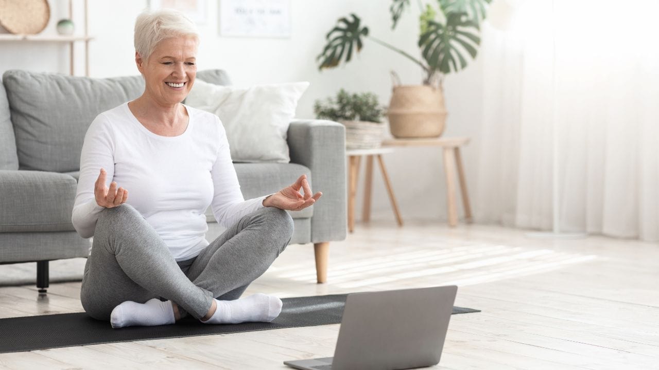 older lady sitting on floor with laptop doing Mindfulness-Based Stress Reduction MBSR technique